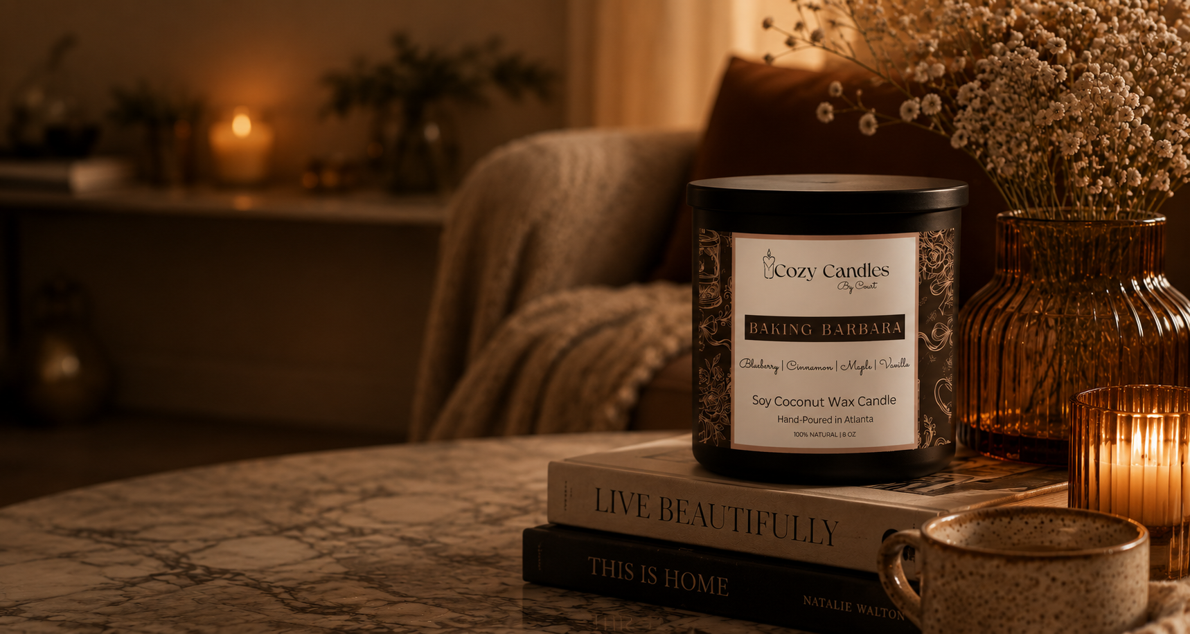 Candle with a label on top of books in a cozy setting with candles and decor.