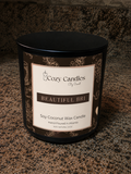 A black soy coconut wax candle by Cozy Candles, titled 'Beautiful Bri', shown on a speckled granite countertop. The candle is in a black metal tin with a cream and dark brown label featuring ornate gold-toned scrollwork.