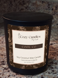 A black glass jar candle with a matching lid and a cream label reading 'Cozy Candles by Scents COOL CO Soy Coconut Wax Candle' on a speckled granite countertop.