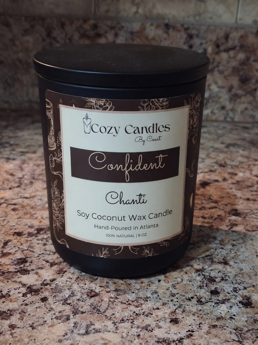 A black jar candle labeled 'Cozy Candles By Cozy Court' and 'Confident Chanti' soy coconut wax candle, placed on a speckled granite countertop.