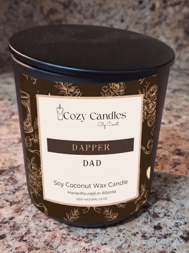 A Cozy Candles 'Dapper' soy coconut wax candle in a dark brown and black glass jar with a cream label, set on a speckled granite countertop.