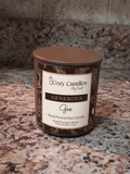 A Cozy soy candle in a brown glass jar with a matching brown lid and a cream label reading 'Generous Gee'. The candle is placed on a speckled granite countertop with a tiled backsplash behind it.