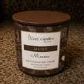 A Cozy Candles 'Meme Mimosa' soy coconut wax candle in a brown metal tin with a white and brown label, sitting on a speckled granite countertop.