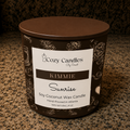 A 16 oz soy coconut wax candle by Cozy Candles in the 'Kimmie Sunrise' scent, in a dark brown metal tin with a white label, sitting on a granite countertop.