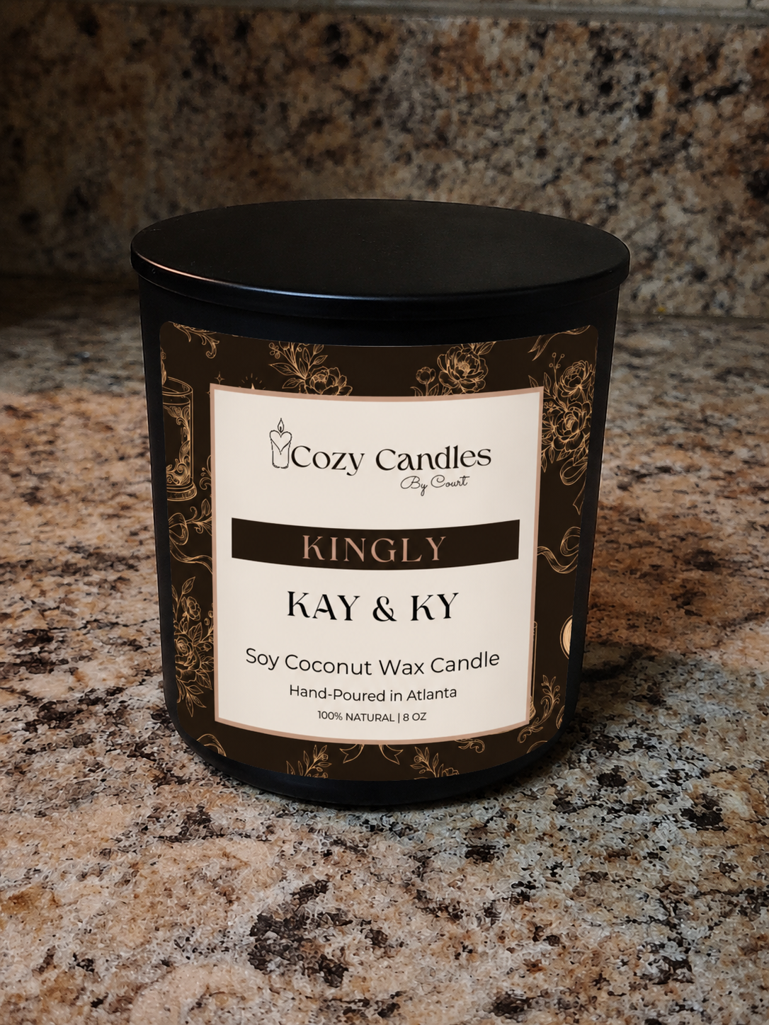 A black metal candle jar with a black lid and a cream label reading 'Cozy Candles City Scent' and 'Kingly Kay & Ky Soy Coconut Wax Candle,' placed on a speckled granite countertop.
